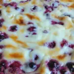 Valkosuklainen marjarahkapiiras leikattuna lusikalla mustikoita ja vadelmia